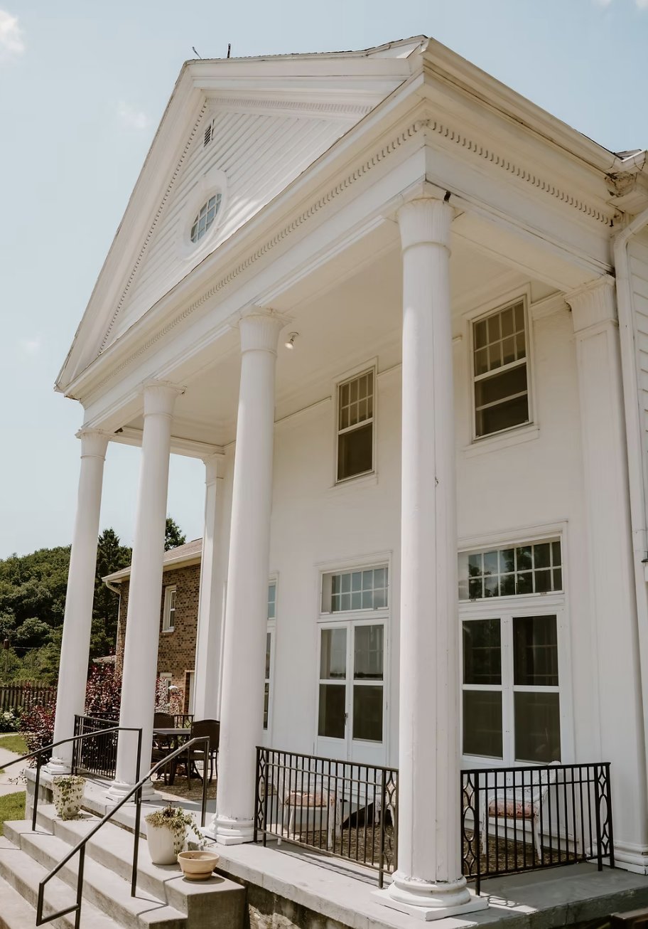 The white-columned front porch of the Abbey at Otter Creek on a sunny day